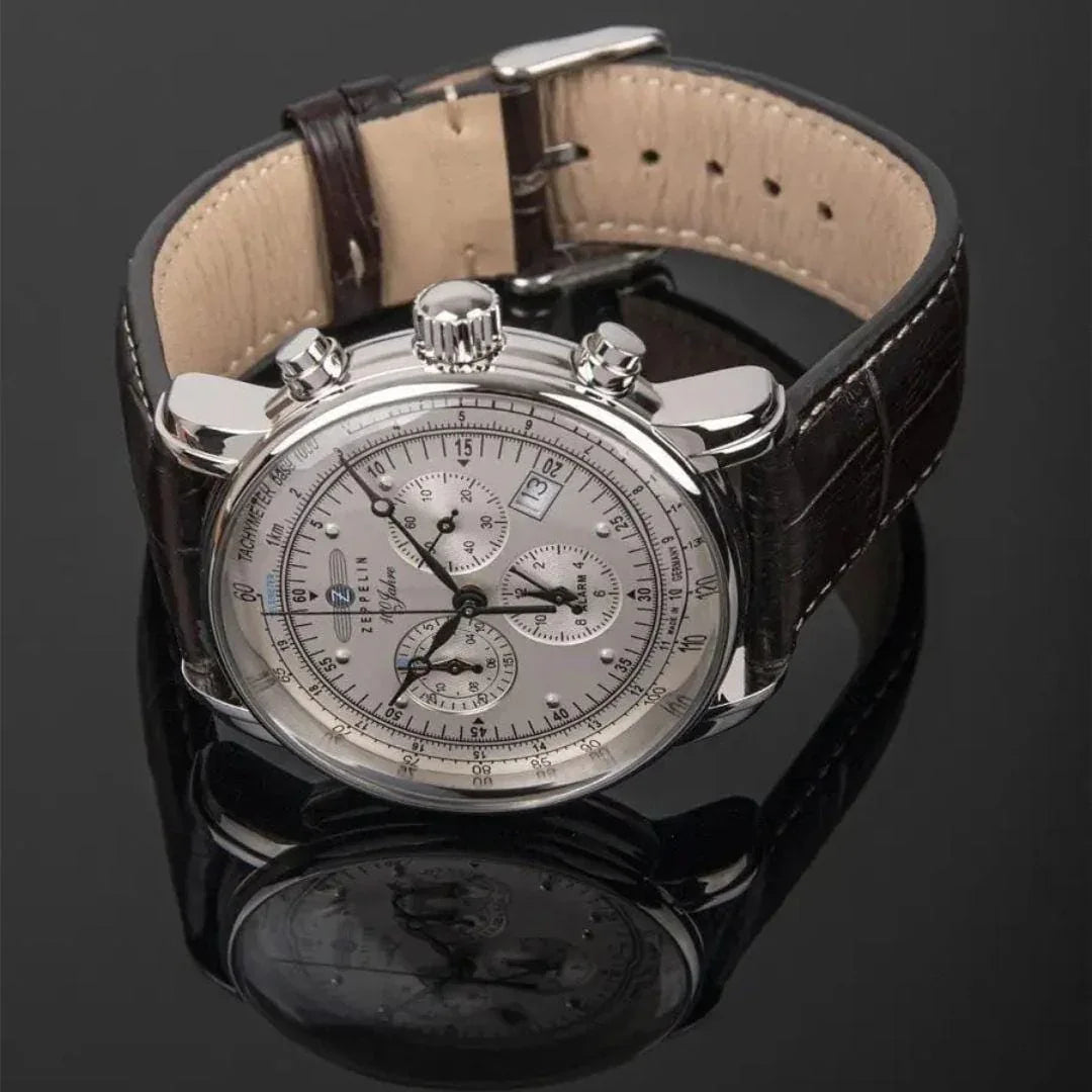Luxury men's silver chronograph watch with brown leather strap on black reflective surface