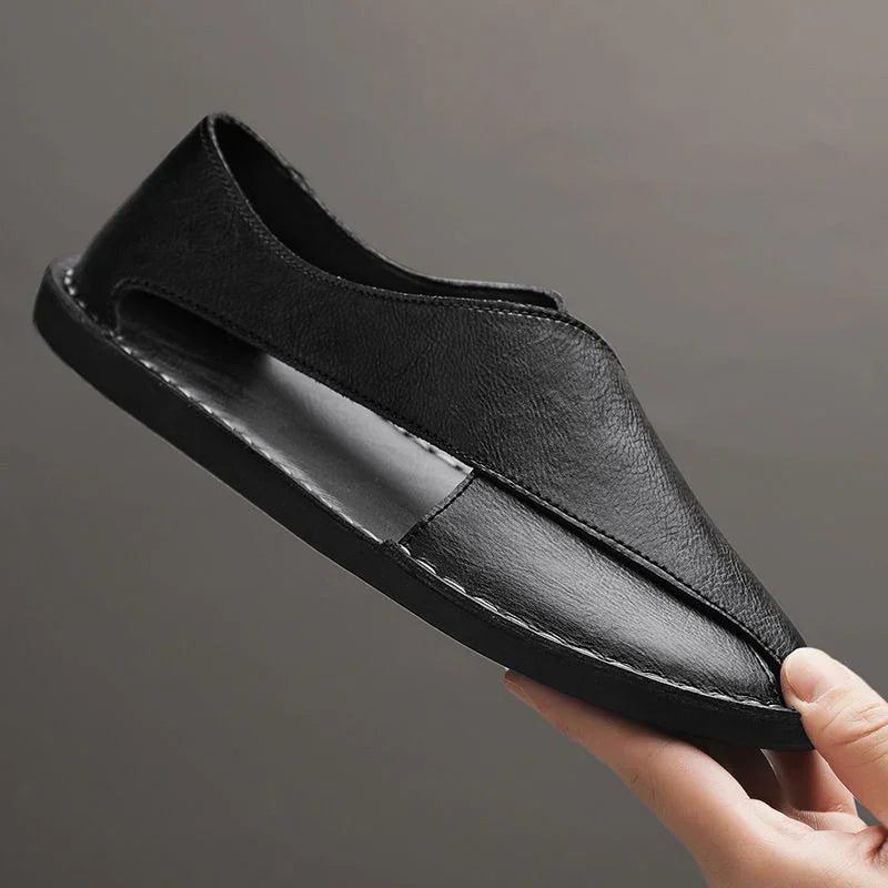 Hand holding a black leather sandal with sleek stitching, minimalist design, Auretier footwear