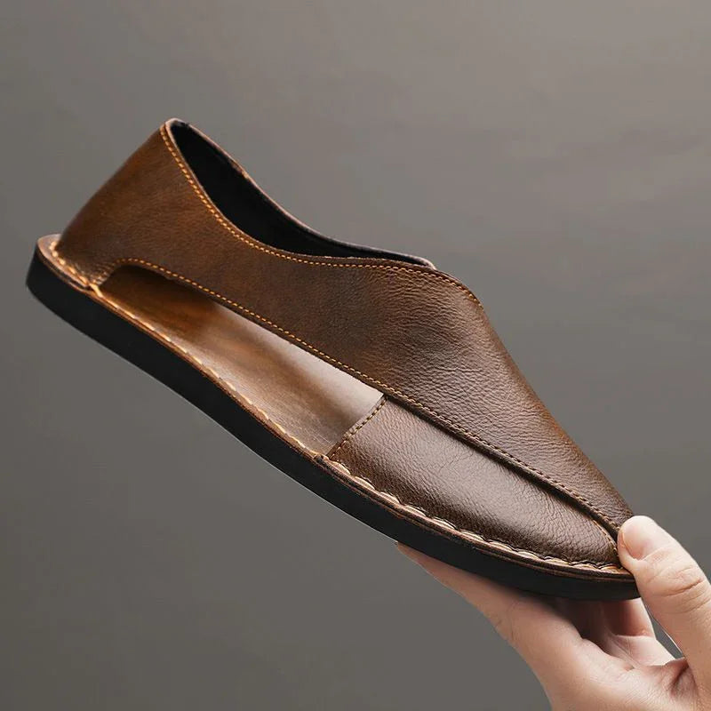 Auretier brown leather sandal with cut-out sides and black sole, held against a gray background.