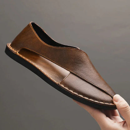 Auretier brown leather sandal with cut-out sides and black sole, held against a gray background.